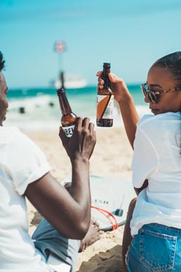 students drinking beer on the beach with the sea opposite